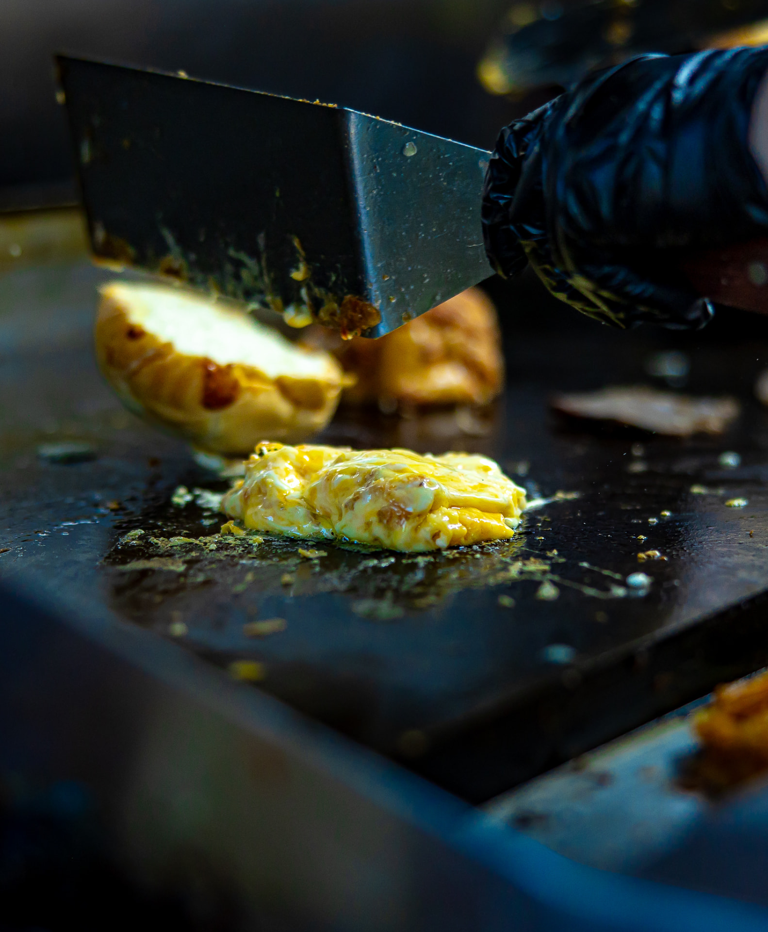 A spatula pressing a pile of melting cheese next to toasted bread on the griddle